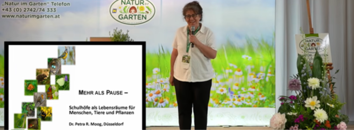 Dr. Petra Regina Moog steht mit einem Mikrofon vor dem Publikum und referiert zu dem Thema "Mehr als Pause". Dieser Satz ist mit dem Untertitel "Schulhöfe als Lebensräume für Menschen, Tiere und Pflanzen" unten links eingeblendet. Foto: Stefanie Weber